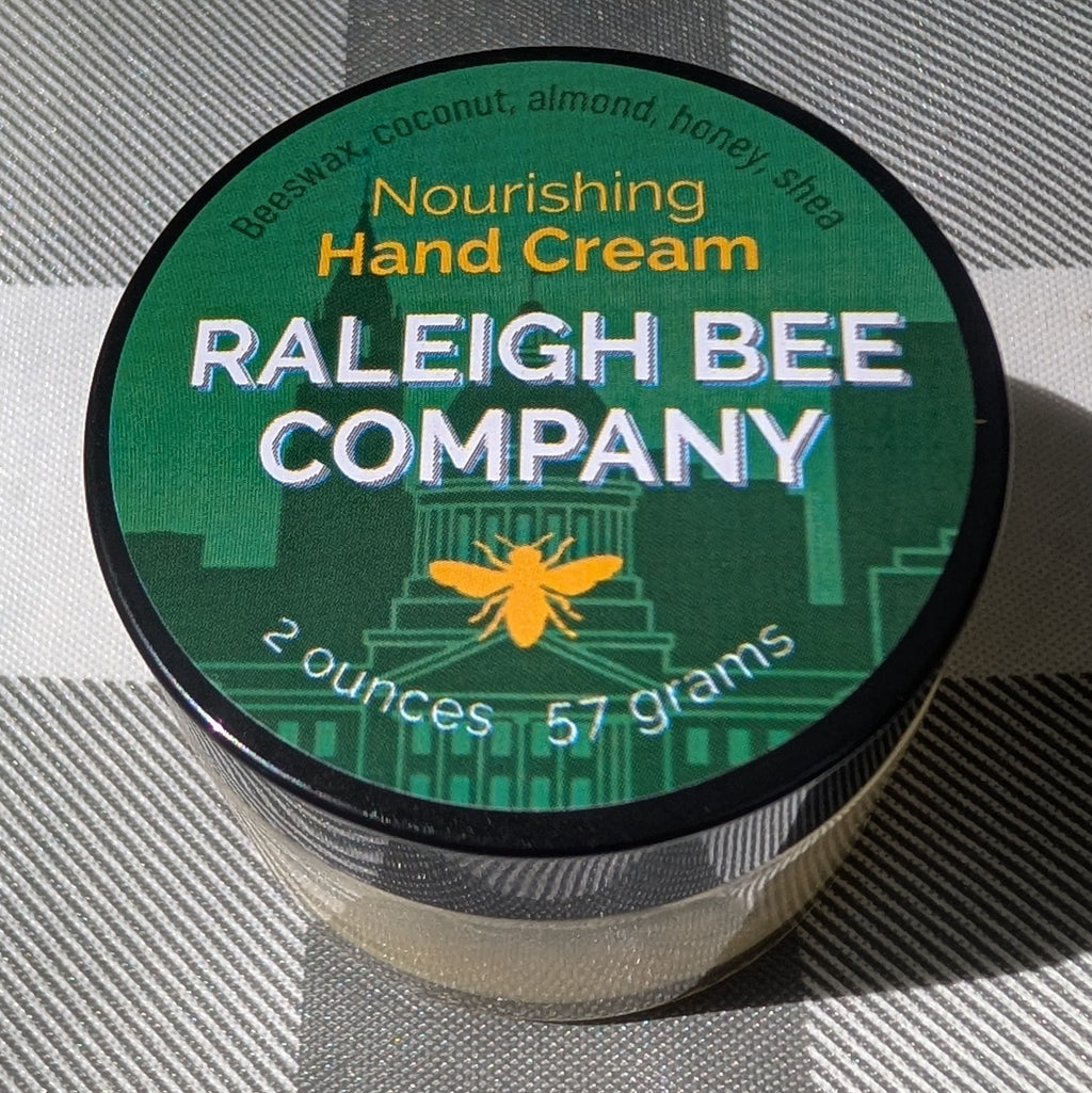 Jar of Raleigh Bee Company hand cream on a checkered fabric background. Contains: Beeswax, coconut oil, almond oil, honey, and shea butter.