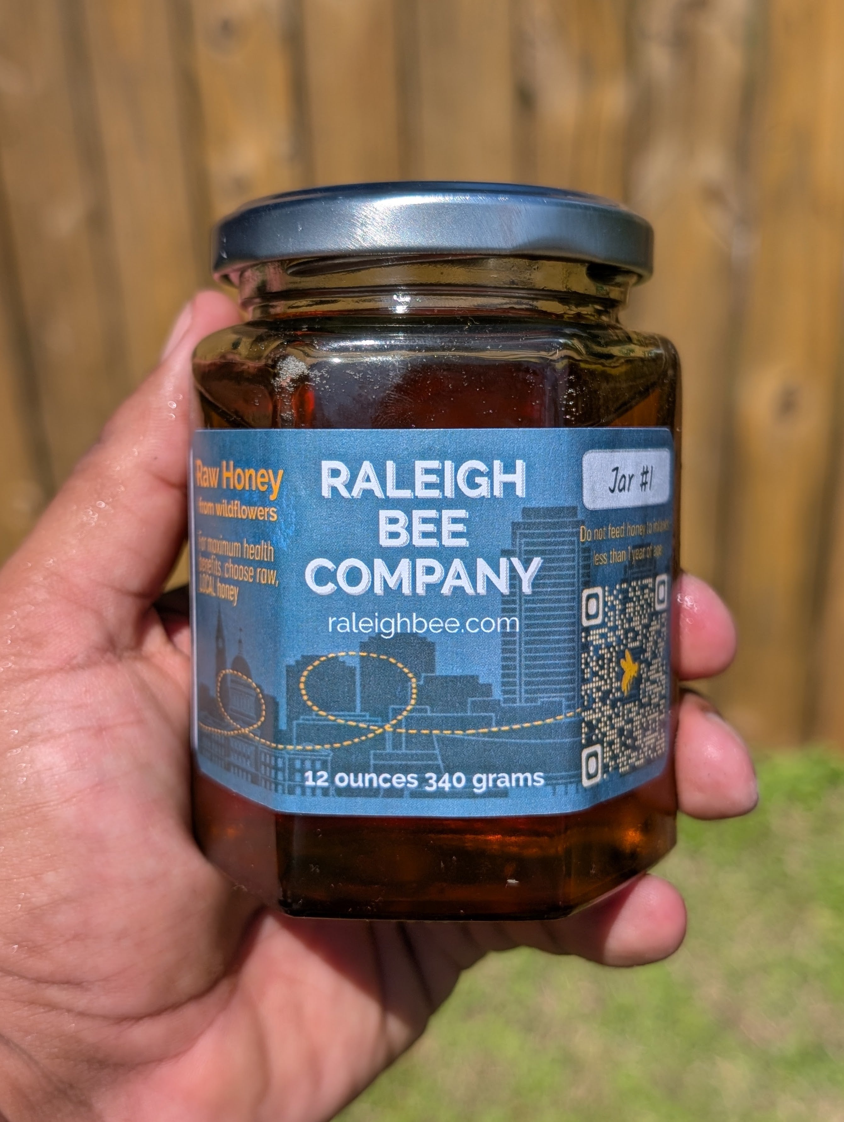 12 oz hexagonal jar of honey from Raleigh Bee Company held in a hand with a blurred background