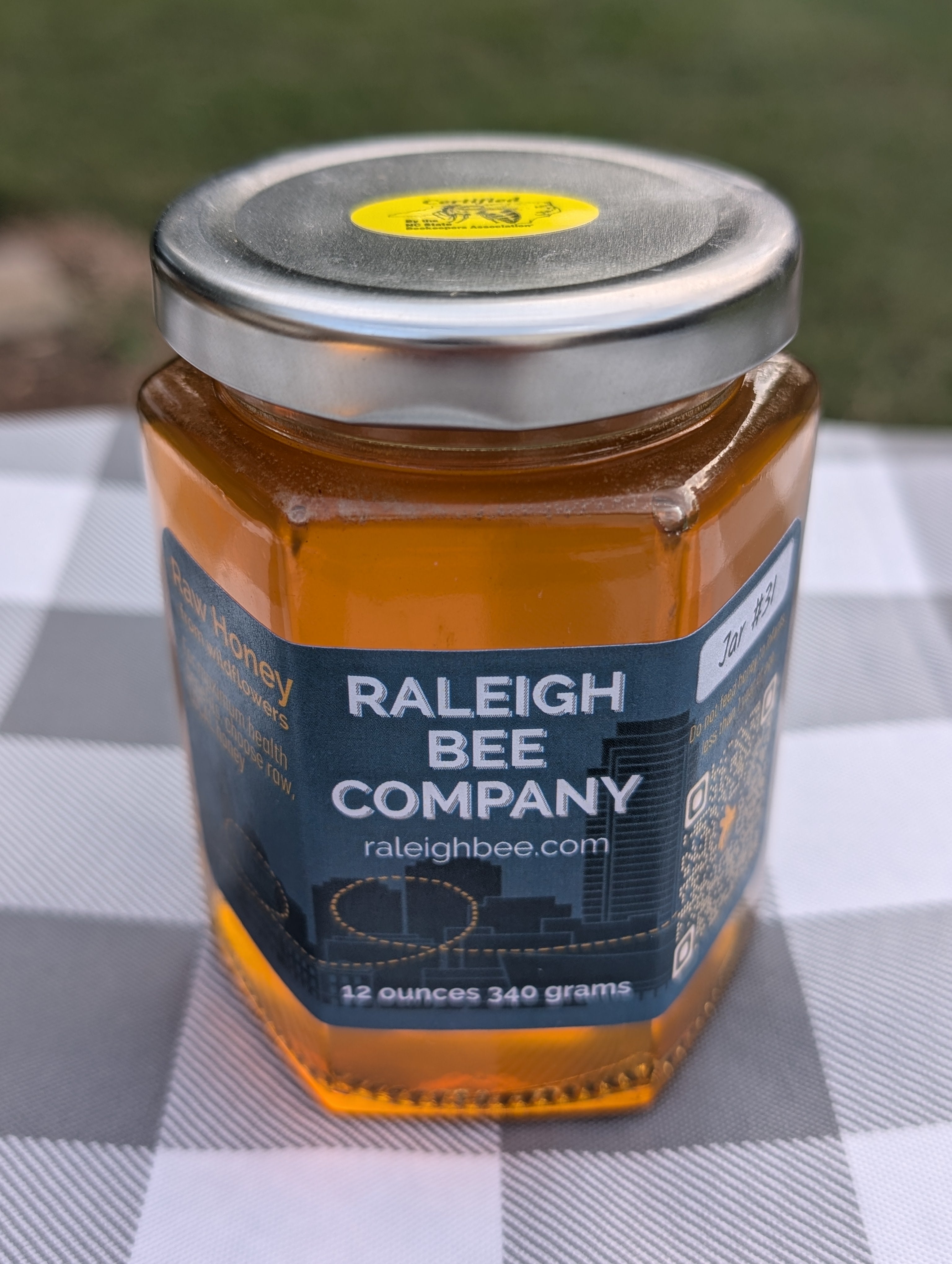 12 oz hexagonal jar of honey from Raleigh Bee Company on a checkered tablecloth.
