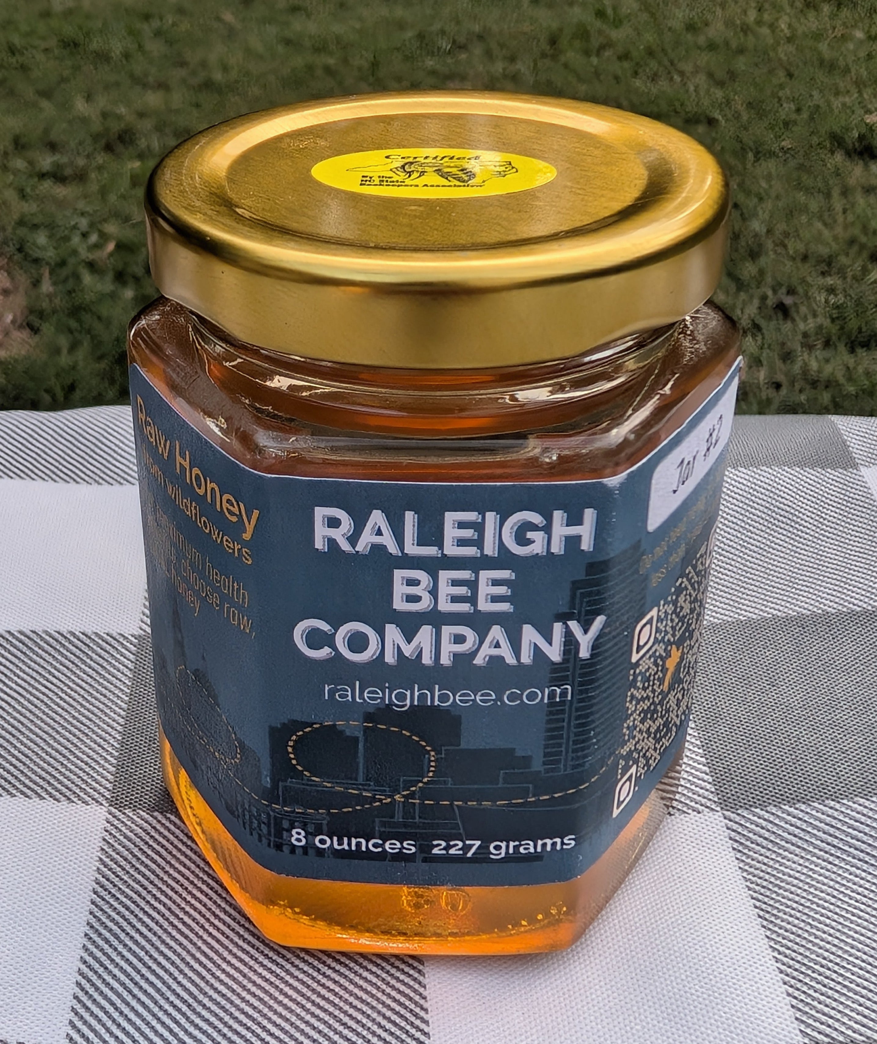 8 oz hexagonal jar of honey from Raleigh Bee Company on a checkered tablecloth