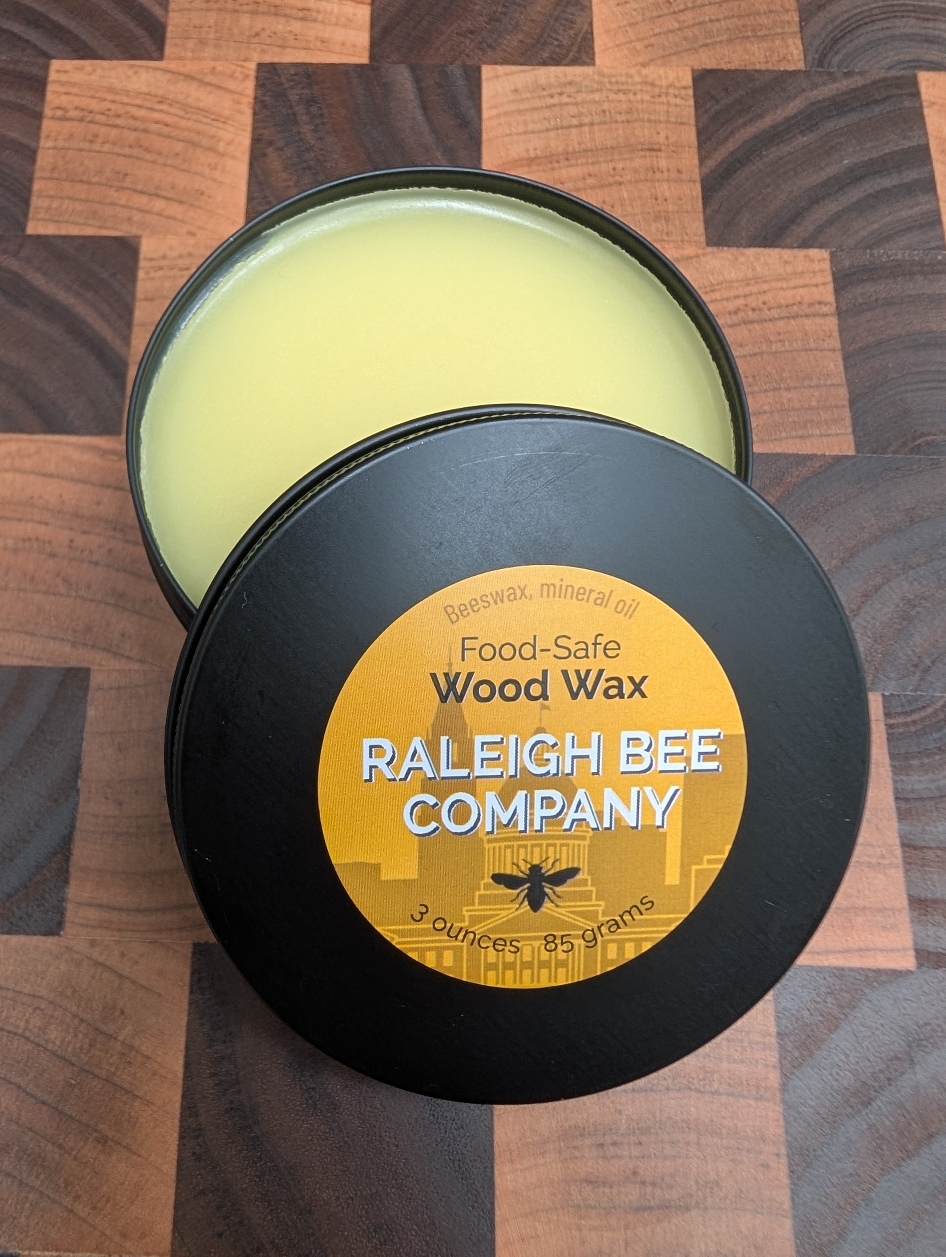 Metal tin of Raleigh Bee Company wood wax on a checkered wooden surface.